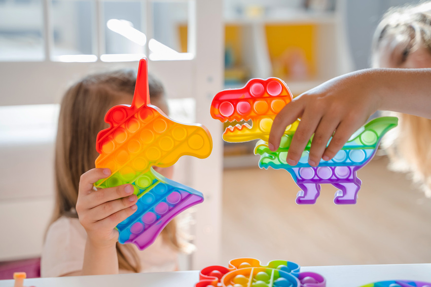 Two children play with rainbow-colored toys, one unicorn and one dinosaur, in a waiting room