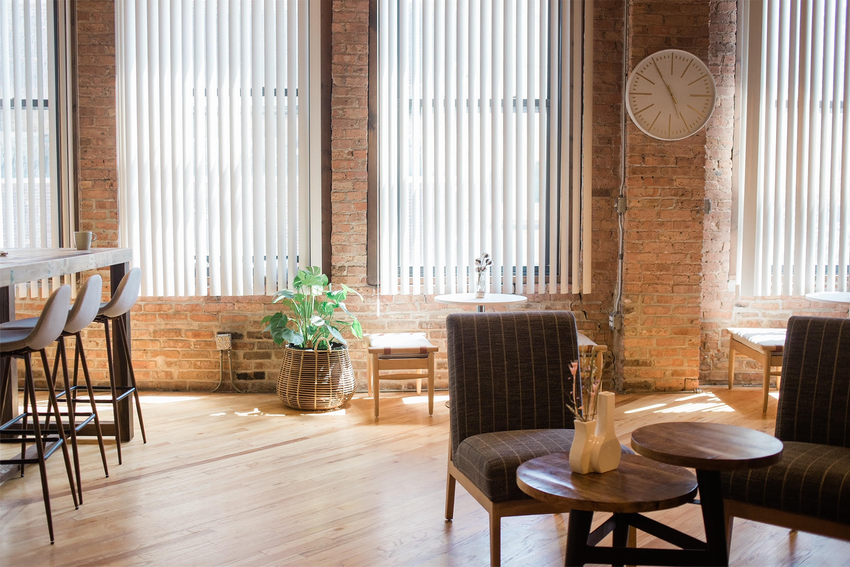 The main coworking space at Chicago Minds. A table and two chairs are in front of the exposed brick walls and windows. To the left, there is a countertop with barstools.