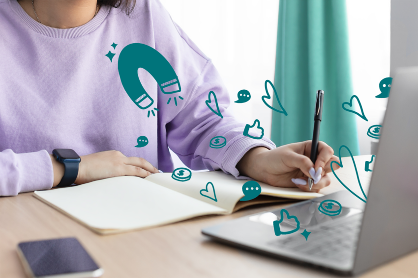 A person wearing a purple sweater sits at their laptop and writes in a notebook while an illustration shows a magnet pulling dollars, hearts, messages, and thumbs up icons out of the screen